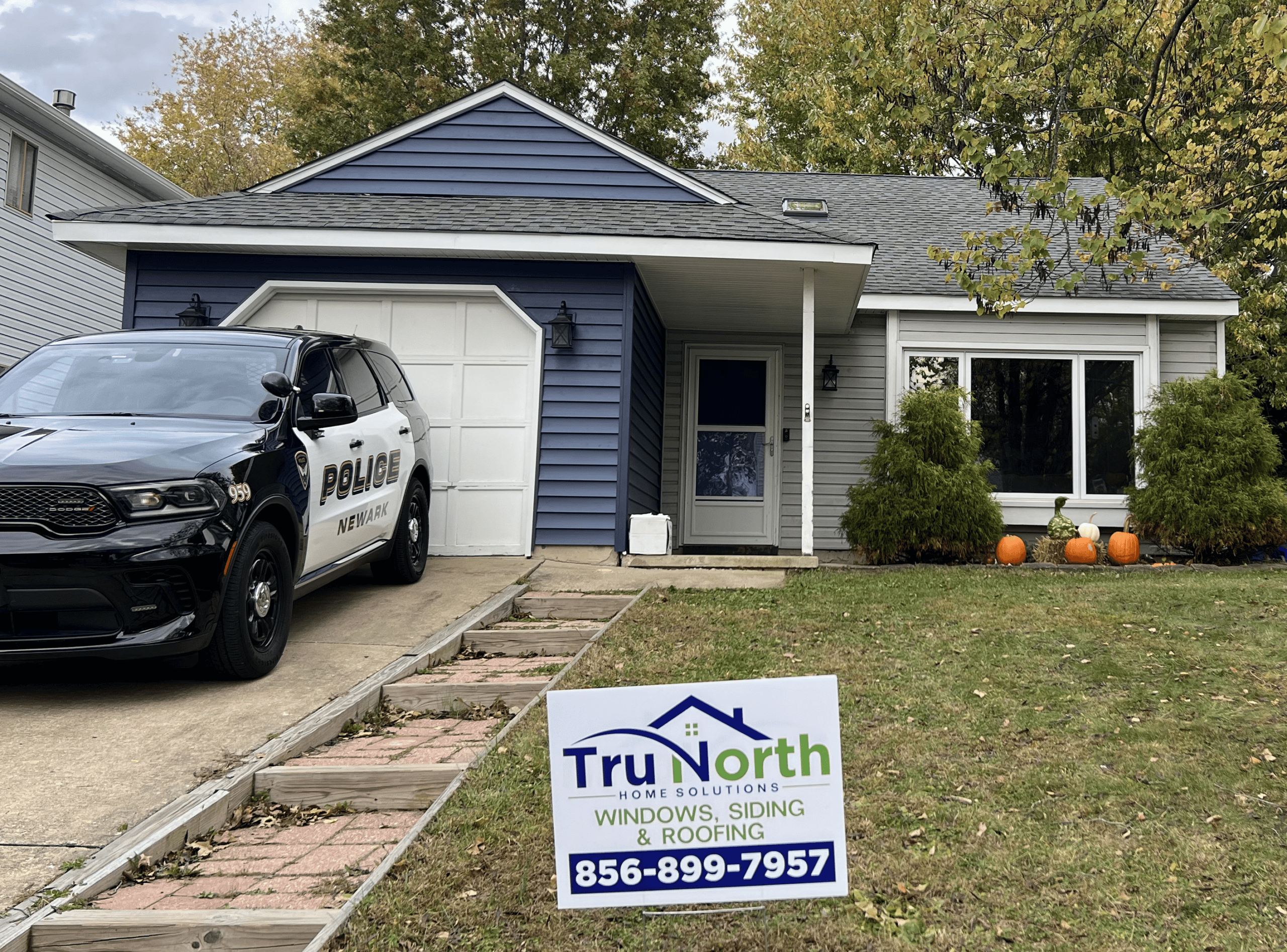Example Co Home Exterior Home with blue siding, police car, and Trunorth sign in yard for window and roofing services.